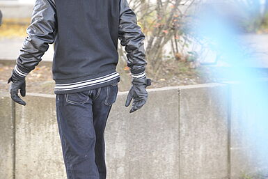 Junger Mann von hinten mit Lederjacke und Lederhandschuhen.