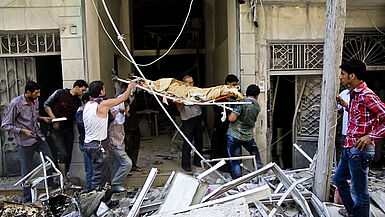 Junge Männer in Aleppo, Syrien tragen einen Leichnam aus einem zerstörten Gebäude