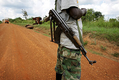 Junge in Militärhosen mit Gewehr.