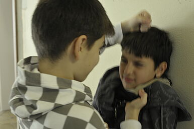 Junge bedrängt einen anderen Jungen, packt ihn am Kragen und stößt ihm mit der Faust auf den Kopf.